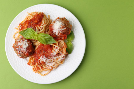 Delicious pasta with meatballs, cheese and basil on green table, top view. Space for textの写真素材