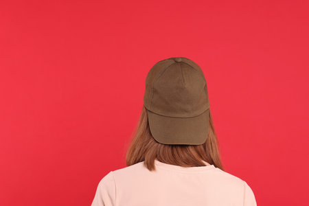 Woman in stylish baseball cap on red background, back view. Mockup for designの写真素材