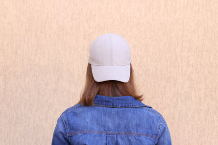 Woman in stylish baseball cap near beige wall, back view. Mockup for designの写真素材
