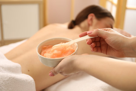 Esthetician applying cosmetic product for body wraps treatment onto woman's back in spa salon, closeupの写真素材