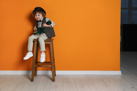 Cute little boy with old telephone on stool near orange wall, space for textの写真素材