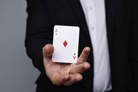 Illusionist with playing card on grey background, closeup