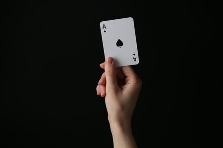 Woman with playing card against black background, closeupの写真素材