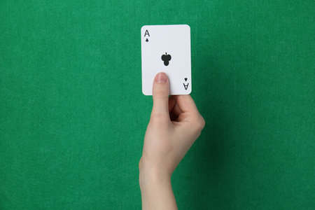 Hand holding playing card against green background, closeupの写真素材