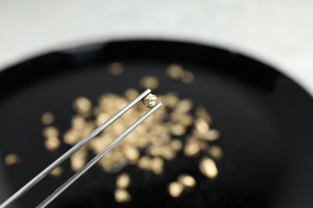 Tweezers with gold nugget against blurred background, closeup. Space for textの写真素材