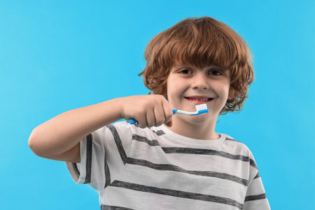 Cute boy with toothbrush on light blue background
