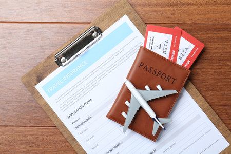 Medical tourism. Travel insurance application form, passport with tickets and airplane model on wooden background, top viewの写真素材
