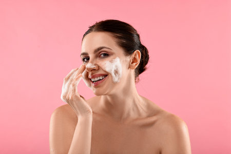 Smiling woman washing her face with cleansing foam on pink backgroundの写真素材