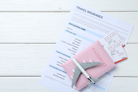 Medical tourism. Travel insurance application form, plane model, passport and flight tickets on white wooden table, top view. Space for textの写真素材
