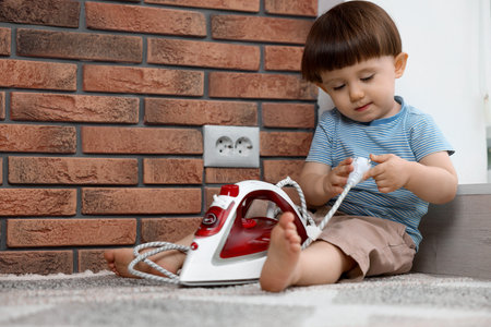 Little boy playing with iron plug near electrical socket at home. Child in dangerの写真素材