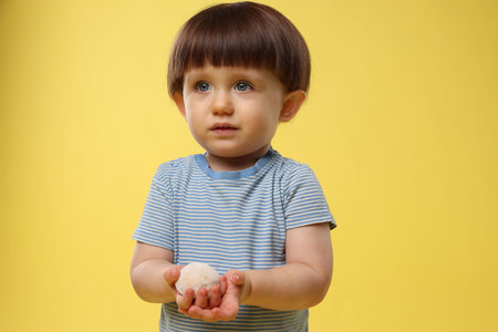 Cute little child with tasty mochi on yellow backgroundの写真素材