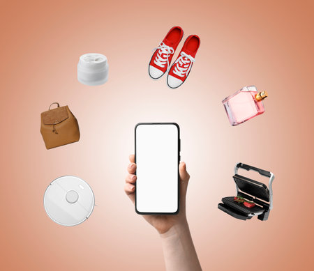 Internet shopping. Woman using mobile phone with blank screen on light brown background, closeup. Different goods flying aroundの写真素材