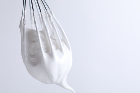 Whisk with whipped cream on white background, closeup. Space for textの写真素材