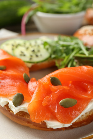 Delicious bagel with salmon, cream cheese, cucumber and pumpkin seeds on table, closeupの写真素材