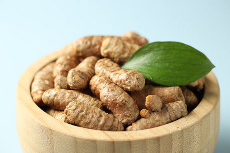 Tumeric rhizomes with leaf in bowl on light blue background, closeupの写真素材