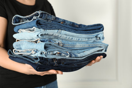 Woman with stack of different stylish jeans near light wall indoors, closeupの写真素材