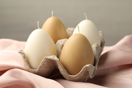 Egg-shaped candles in carton beige fabric against light gray background, closeup. Easter decorの写真素材