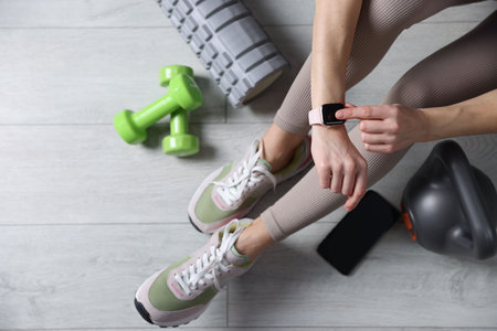 Woman with smart watch, gym equipment and smartphone on floor indoors, top viewのeditorial素材
