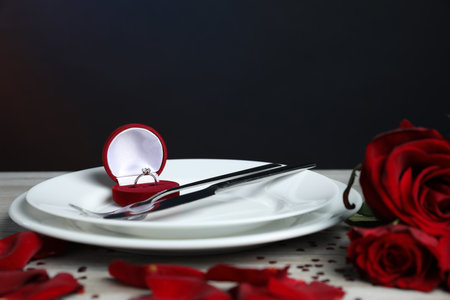 Beautiful setting for romantic dinner and engagement ring surrounded by roses and confetti on light table, closeupの写真素材