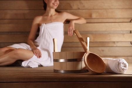 Smiling woman relaxing on bench at sauna, focus on bath suppliesの写真素材