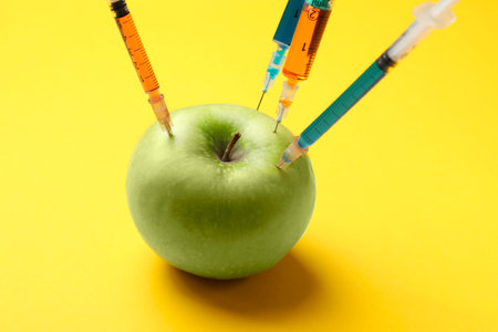 GMO concept. Green apple with different syringes on yellow background, closeup