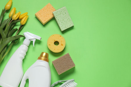 Spring cleaning. Detergents, supplies and tulips on green background, flat lay. Space for textの写真素材