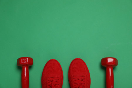Sports equipment. Dumbbells and sneakers on green background, flat lay. Space for textの写真素材