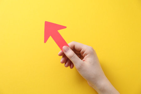 Woman with paper arrow on yellow background, top view