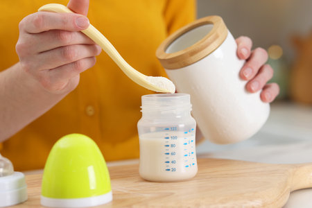 Mother making baby formula in feeding bottle at table indoors, closeupの写真素材