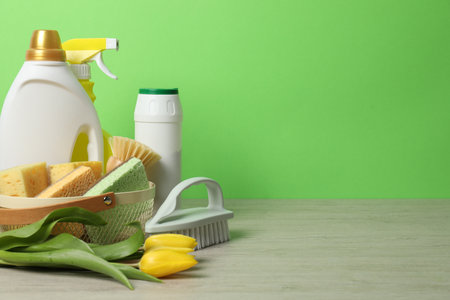 Spring cleaning. Detergents, supplies and tulips on white wooden table against green background, space for textの写真素材