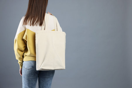Woman with blank shopper bag on gray background, back view. Mockup for design