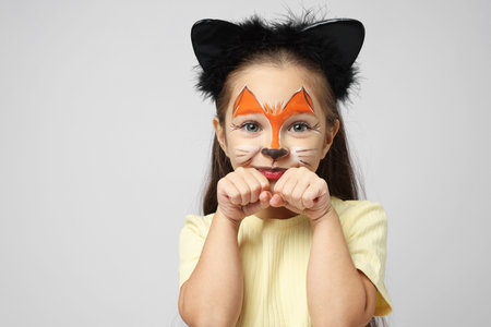 Cute girl with painted face and ears as cat on grey background, space for text