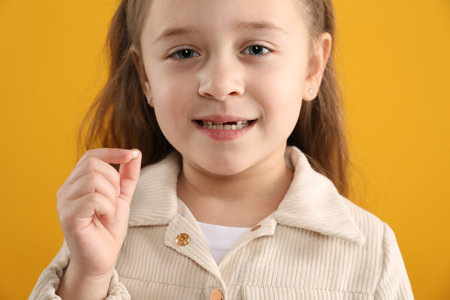 Cute little girl with missing tooth on orange background, closeup. Waiting for tooth fairy