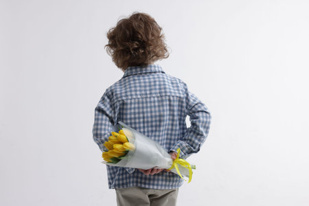 Little boy with bouquet of tulips behind his back on white background