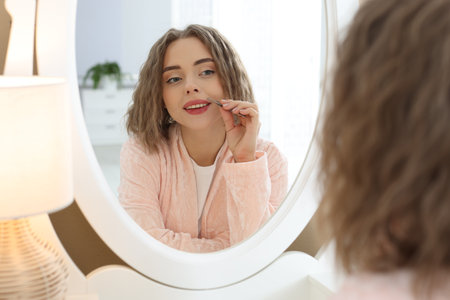 Happy woman plucking her mustache with tweezers near mirror at homeの写真素材