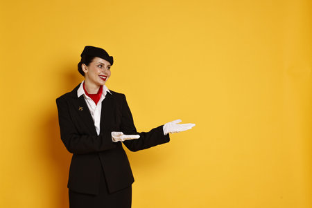 Happy flight attendant showing something on orange background.
