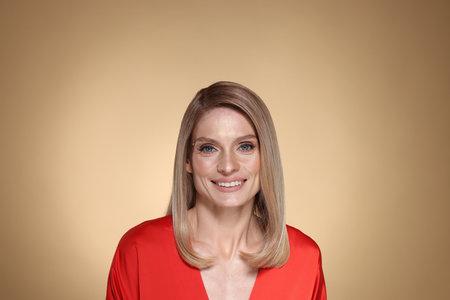 Portrait of beautiful happy woman with straight blonde hair on beige backgroundの写真素材