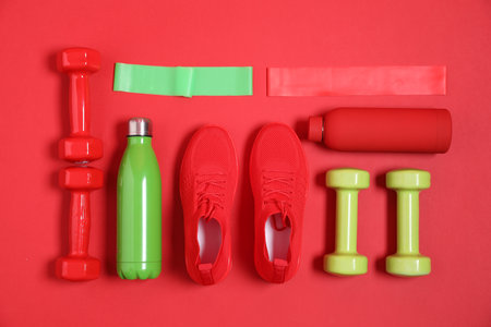 Elastic bands, water bottles, dumbbells and sneakers on red background, flat lay. Sports equipmentの写真素材