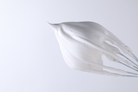 Whisk with whipped cream on white background, closeup. Space for textの写真素材