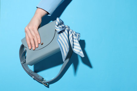 Woman showing stylish handbag on light blue background, closeup. Space for textの写真素材