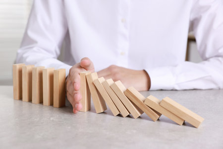 Man stopping wooden blocks from falling at table, closeup. Domino effectの写真素材