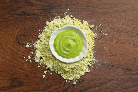Pile of dry wasabi powder and bowl with paste on wooden table, top view