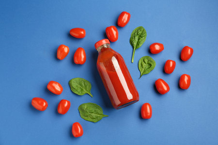 Tasty ketchup in bottle, tomatoes and basil on blue background, flat layの写真素材