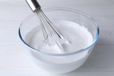 Whisk and bowl of whipped cream on white wooden table, closeupの写真素材