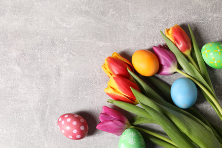 Easter eggs and beautiful tulips on gray table, flat lay. Space for text