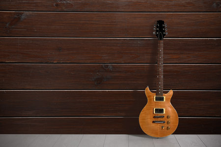 Modern electric guitar on floor near wooden wall. Space for text