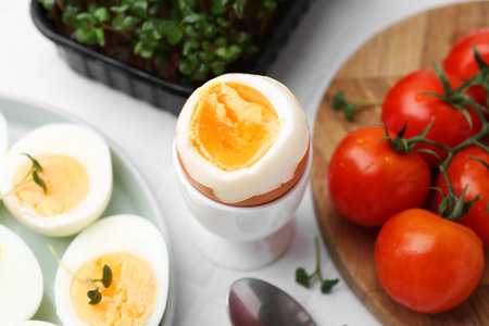 Boiled eggs, tomatoes and microgreens on white tiled table, closeupの写真素材
