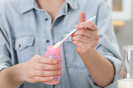 Mother making baby formula in feeding bottle indoors, closeupの写真素材