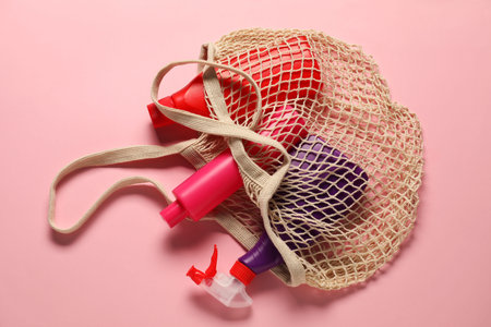 Cleaning products in bag on light pink background, top view