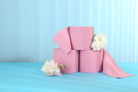 Pink toilet paper rolls and beautiful flowers on light blue background, space for textの写真素材